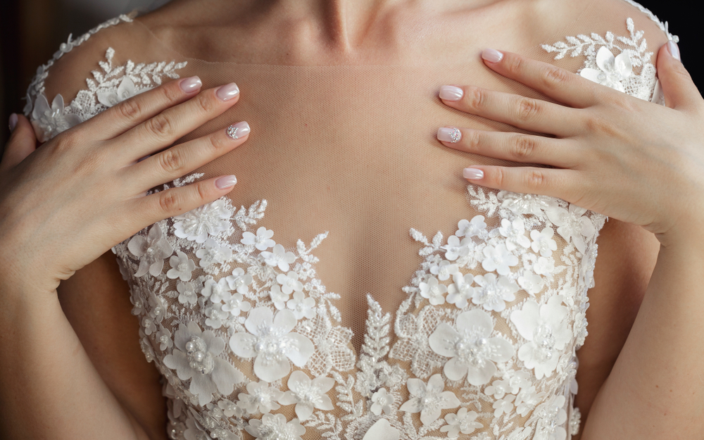 Pessoa com mãos ao colo em um vestido de renda bordado de flores branco